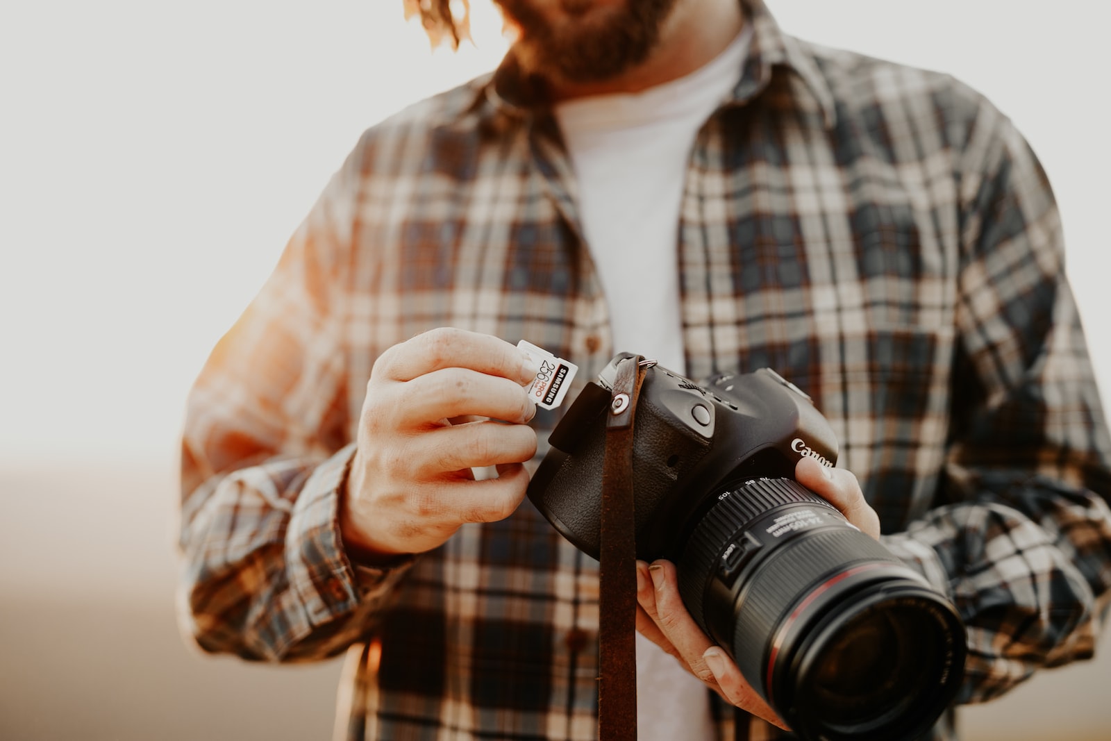 man in red and white plaid dress shirt holding black nikon dslr camera